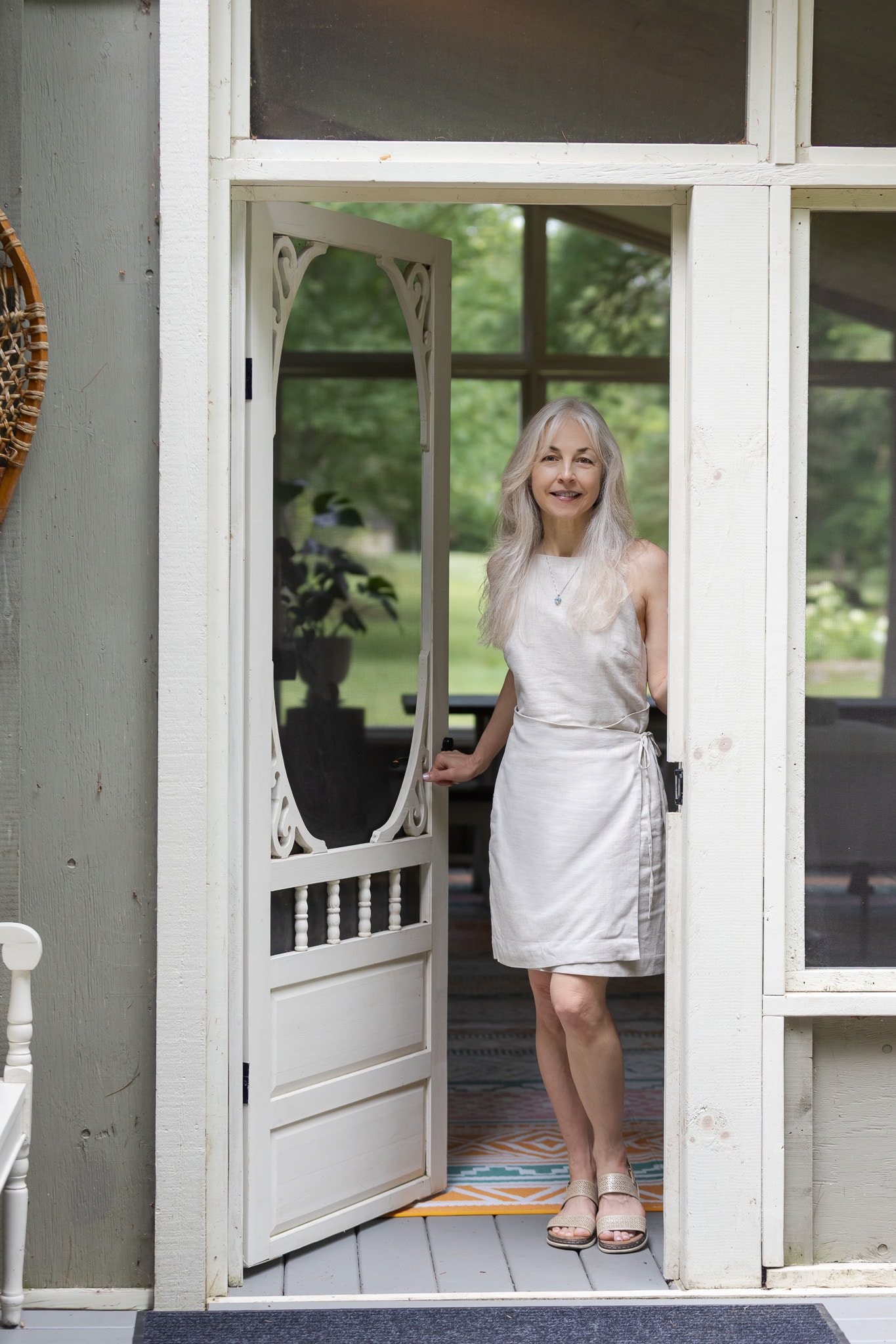 Lori Henein standing in a doorway in a white linen dress, smiling warmly